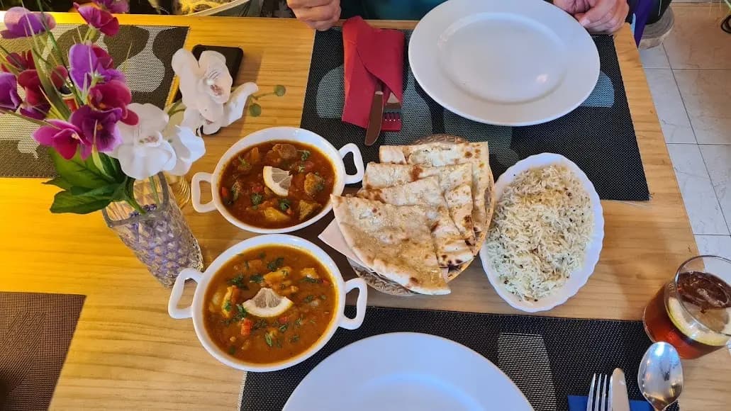 Mesa servida en Royal king indian cuisine en Barcelona con dos cazuelas de curry de pollo, naan troceado, arroz blanco y florero decorativo